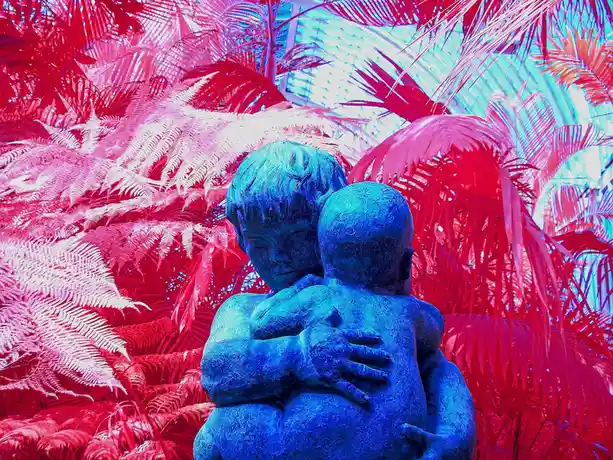 A statue of two children embracing is shown against a background of tropical plants, heavily edited with a red and blue…