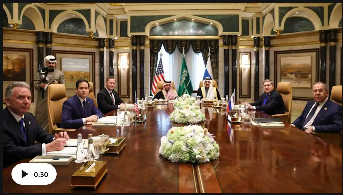 a formal international diplomatic meeting is shown with leaders seated around a long wooden table in an ornate room with…