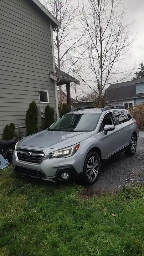 A silver Subaru Crosstrek SUV is parked at an angle on a gravel driveway next to a grassy area, partially on the grass, with…