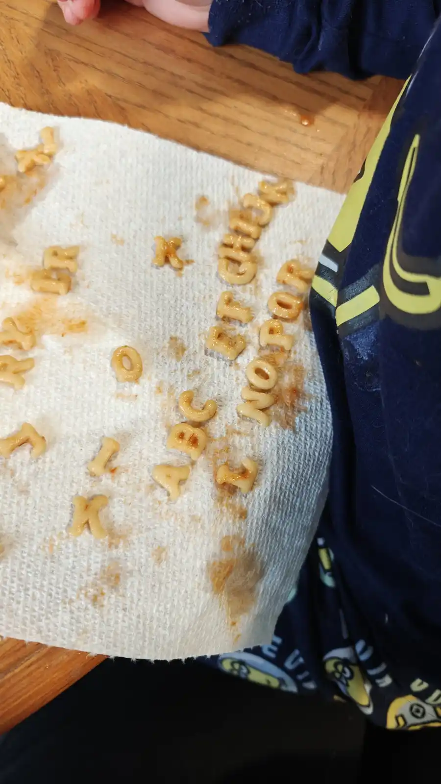 A close-up shot shows alphabet-shaped macaroni letters arranged on a white paper towel, forming the phrase 'chick for nor'…
