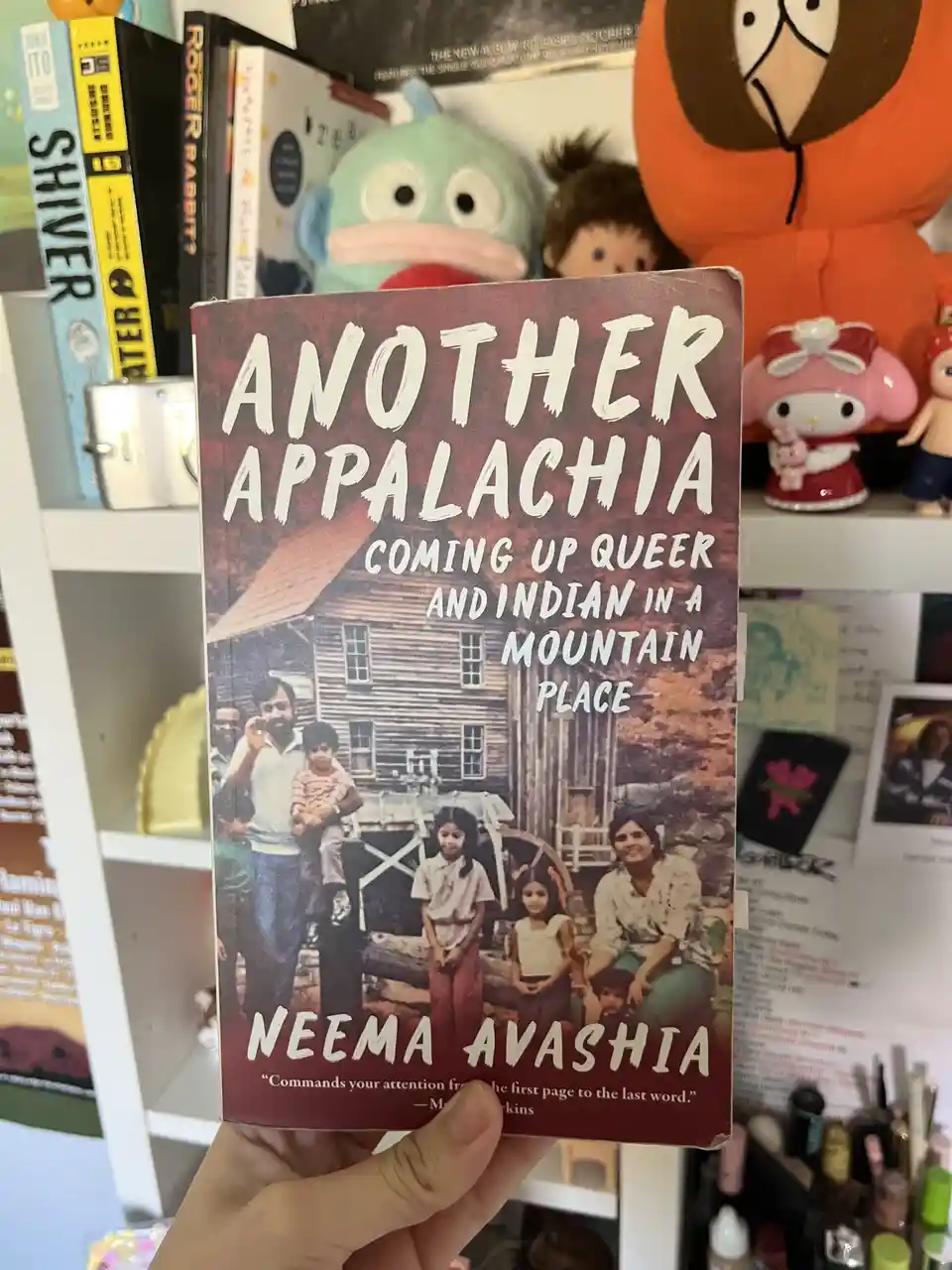 A hand holds up a book titled 'Another Appalachia: Coming Up Queer and Indian in a Mountain Place' by Neema Avashia. The…