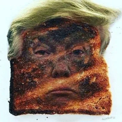 A slice of heavily burnt toast with a charred, distorted face resembling Donald Trump, complete with his signature blond…