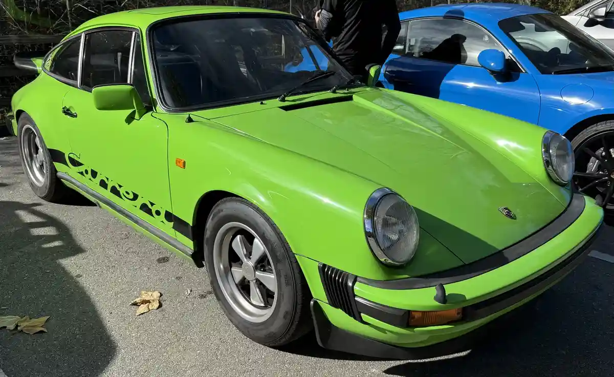 A bright lime green classic Porsche 911 with 'Corona' written in black stylized lettering along its side is parked next to a…