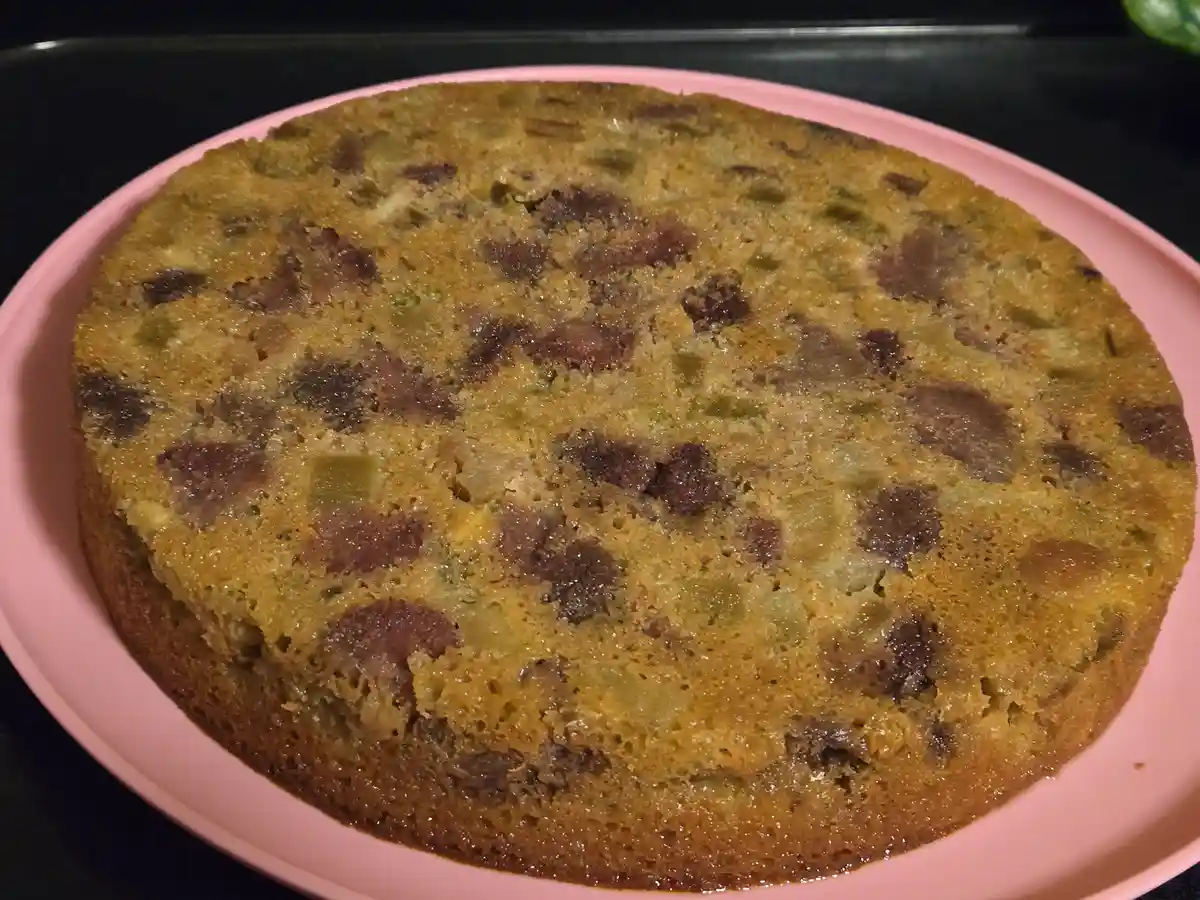 A round, golden-brown baked good sits on a pink plate, visibly containing chunks of green and brown ingredients that…