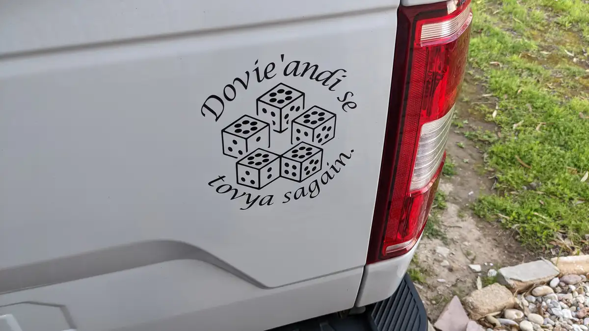 A close-up of a white vehicle's rear door shows a black decal featuring five dice arranged in a cluster, surrounded by the…