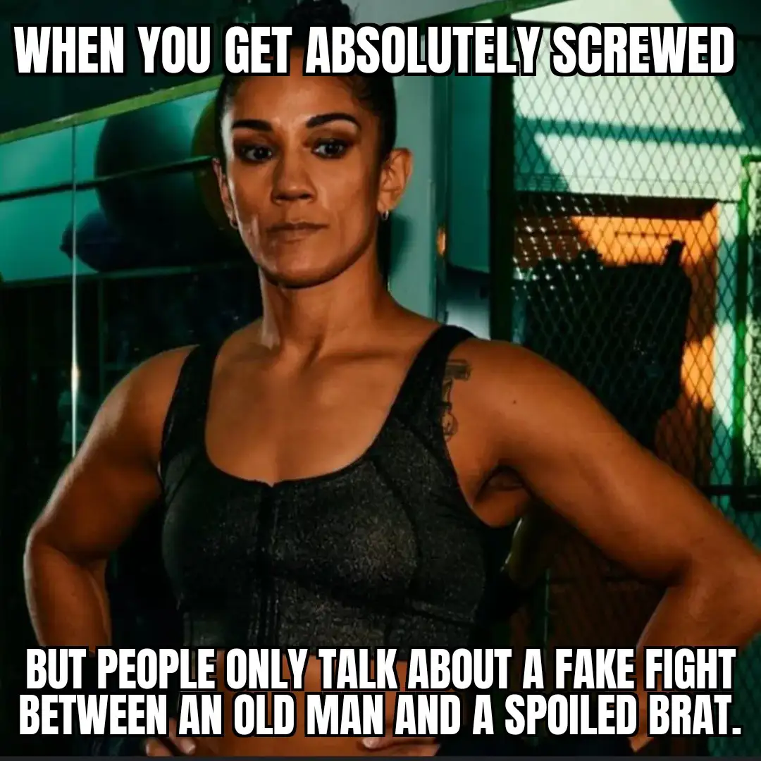 A muscular woman with a stern, unimpressed expression stands with her hands on her hips in what appears to be a gym or…