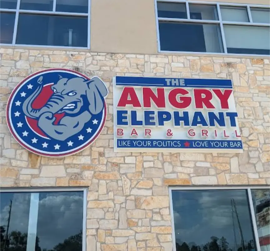 A photo of a bar's exterior sign showing a circular logo with a gray, angry-looking elephant against a red and blue…