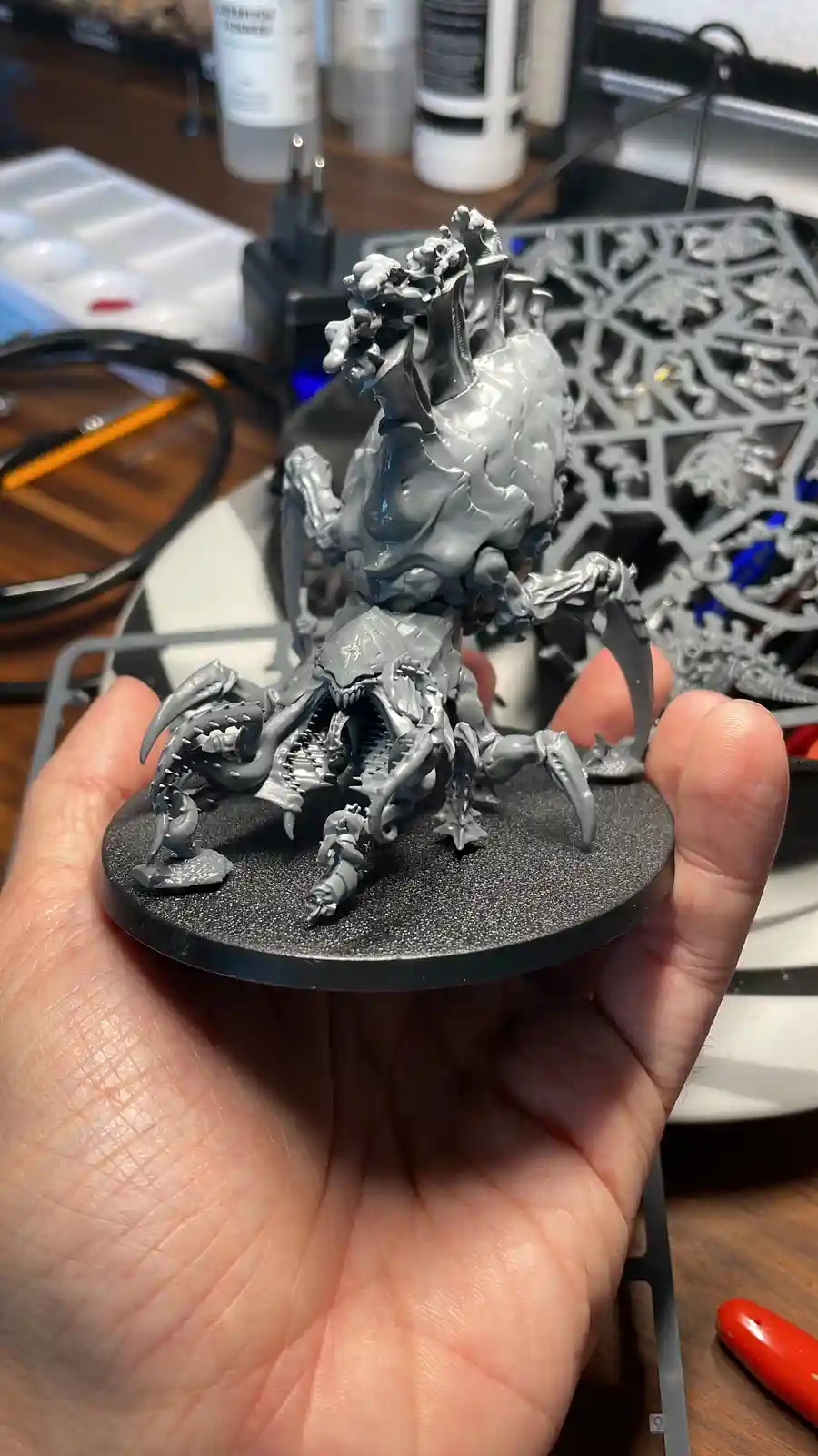 A person holds a freshly printed, unpainted grey resin miniature of a monstrous, multi-limbed creature with a spiked…