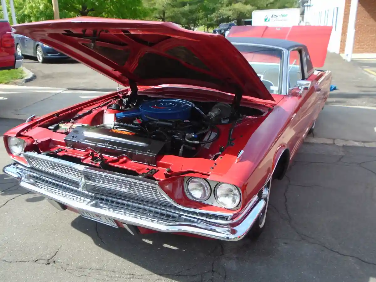 A red classic American car with its hood open, revealing a detailed engine bay with a blue air cleaner and chrome accents…