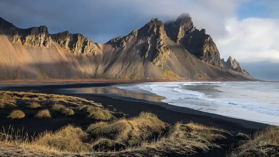 Vestrahorn mountain rises from Iceland's remote southeast coast, its jagged peaks shrouded in mist. Black sands meet the…