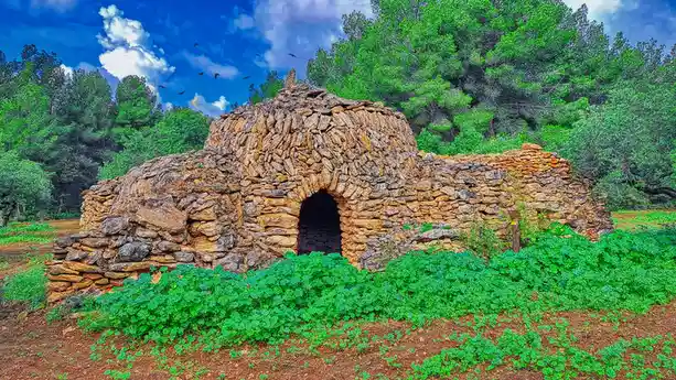 A rustic stone structure with an arched doorway, surrounded by vibrant green foliage and trees under a bright blue sky with…