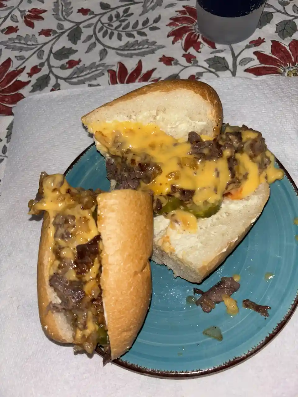 A partially eaten cheeseburger-style sandwich with melted cheese and meat is shown on a blue plate, with the top half…