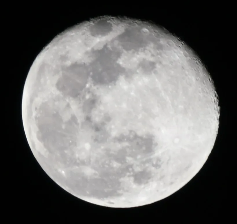 A close-up photograph of the moon against a black sky, showing its cratered surface and grayish-white tones. Overlaid text…