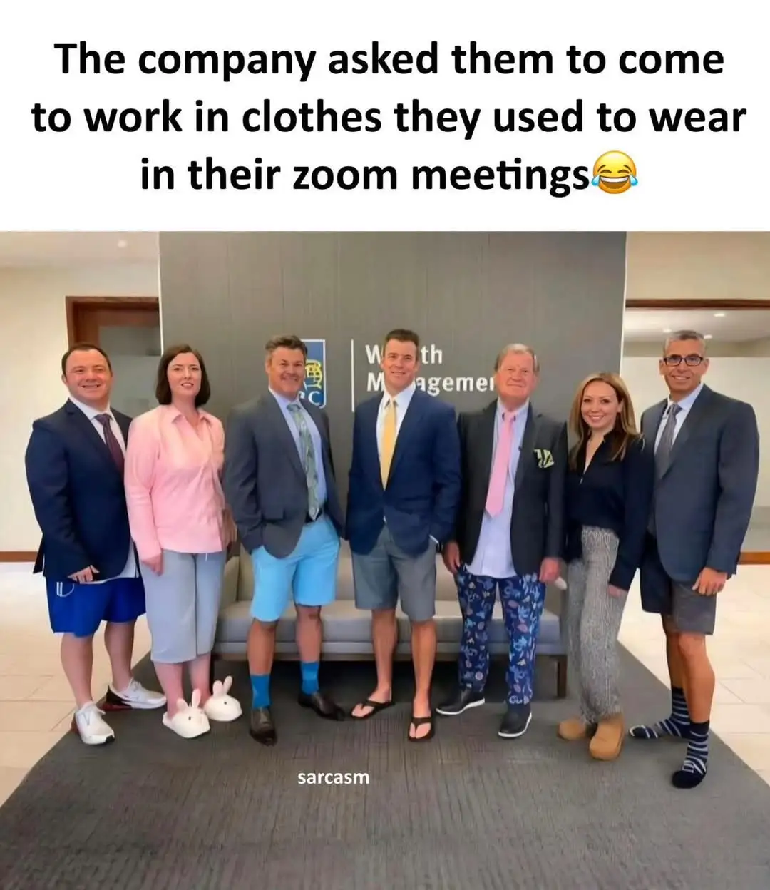 Seven people in a corporate office setting pose for a photo, but their outfits are mismatched and casual, including shorts…