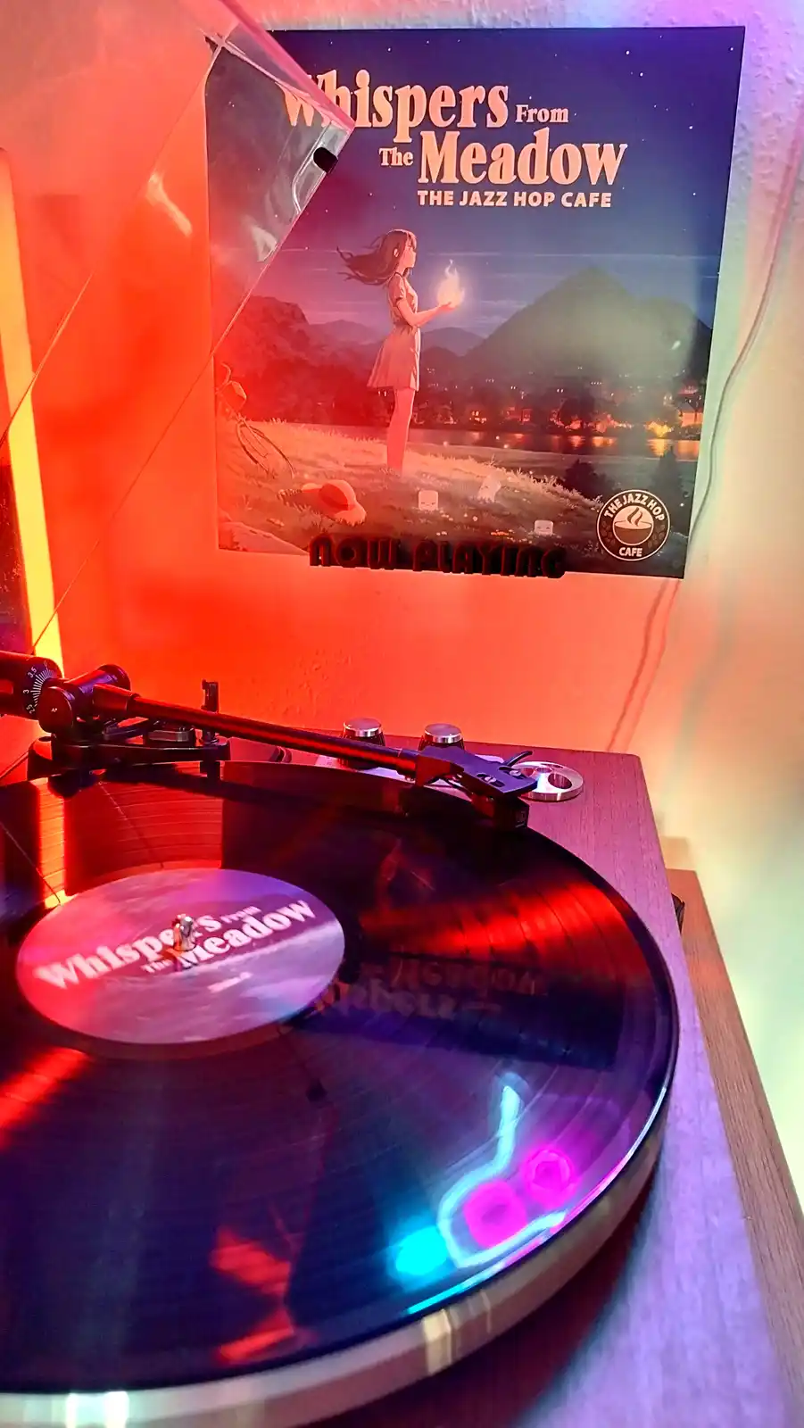 A vinyl record titled 'Whispers From The Meadow' by 'The Jazz Hop Cafe' spins on a turntable under colorful LED lights, with…