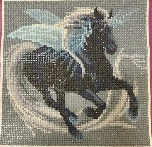 A completed bead art piece depicting a dark horse with wings, rendered in shades of blue, gray, and white beads. The image…
