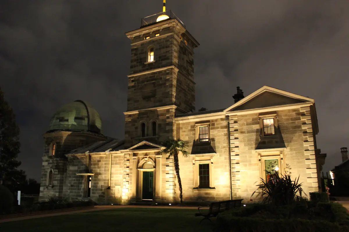 A nighttime photo of a stone observatory building with a prominent tower and a green dome, illuminated by spotlights against…