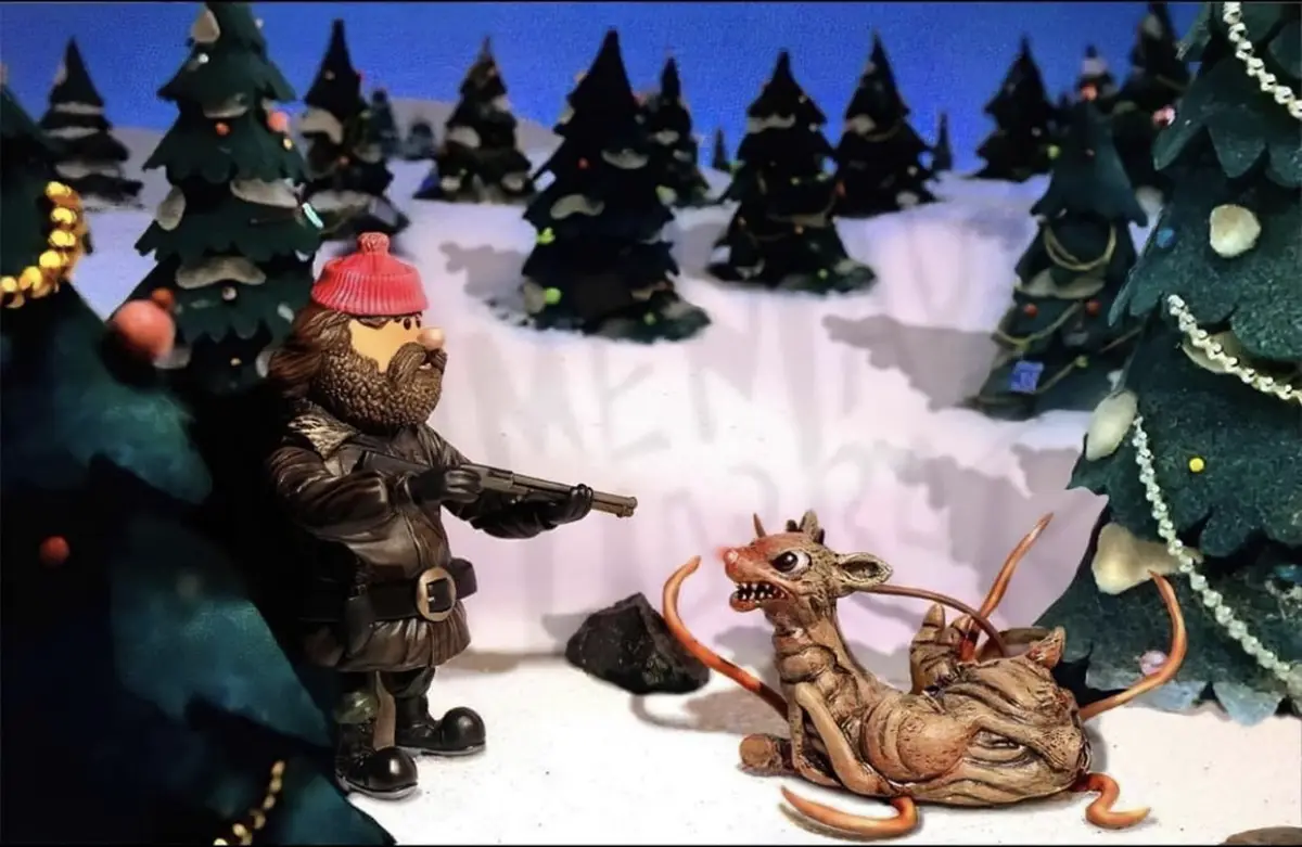 A diorama-style image shows a figurine of a bearded man in a red hat and winter coat holding a rifle, aiming at a grotesque…