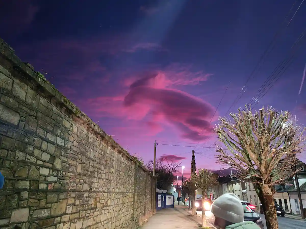 A person in a grey beanie looks up at a dramatic purple and pink sky where a large, fluffy cloud has a distinct shape…