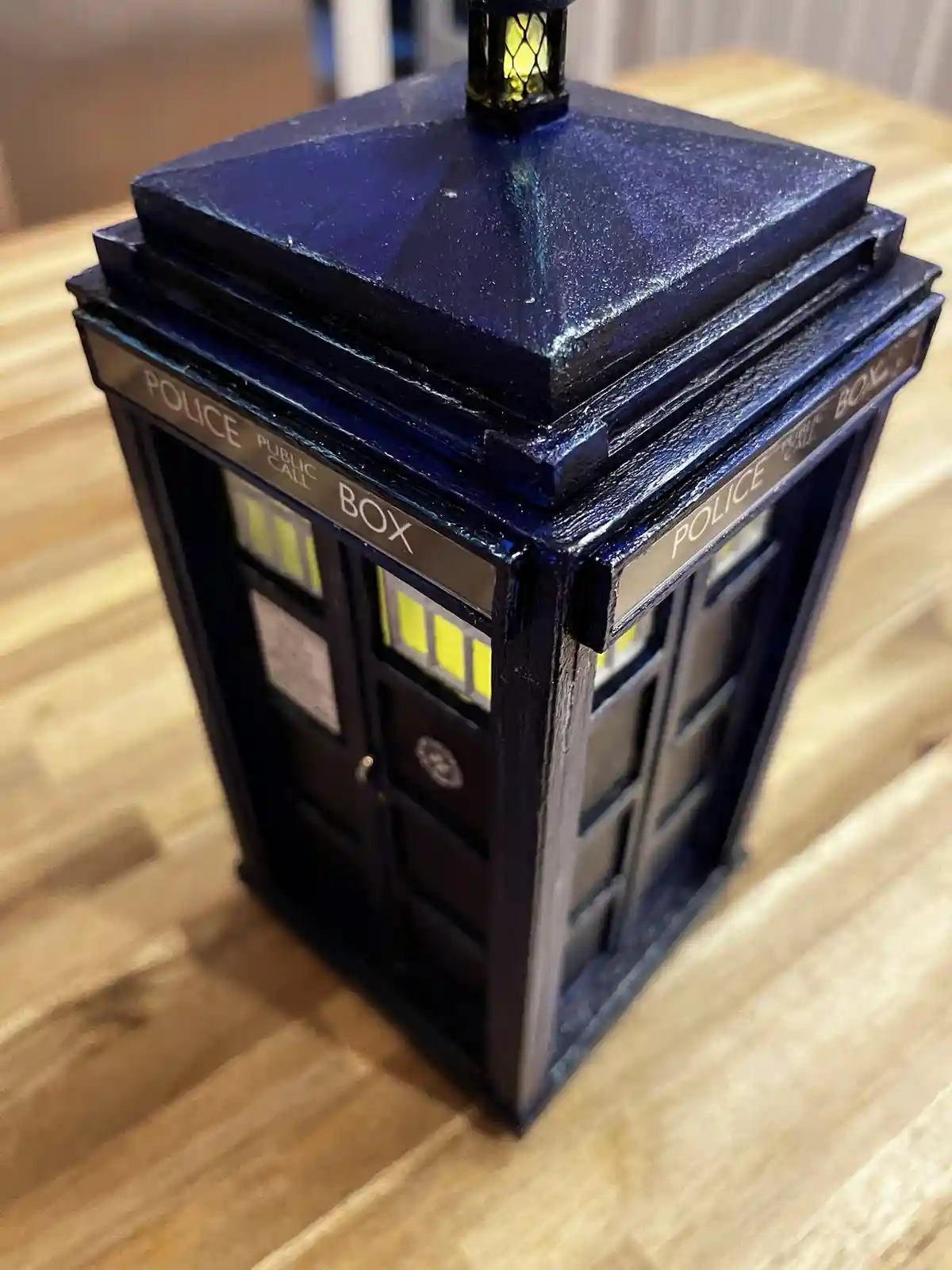 A small, blue, handmade model of a British police public call box, resembling the TARDIS from Doctor Who, sits on a wooden…