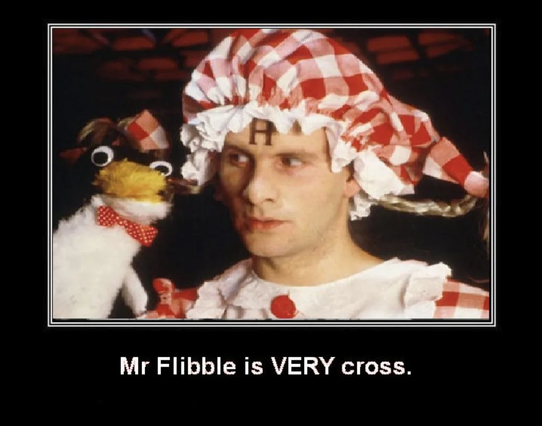 A man in a red-and-white checkered bonnet with a wooden 'H' on his forehead, wearing a matching checkered outfit with a red…