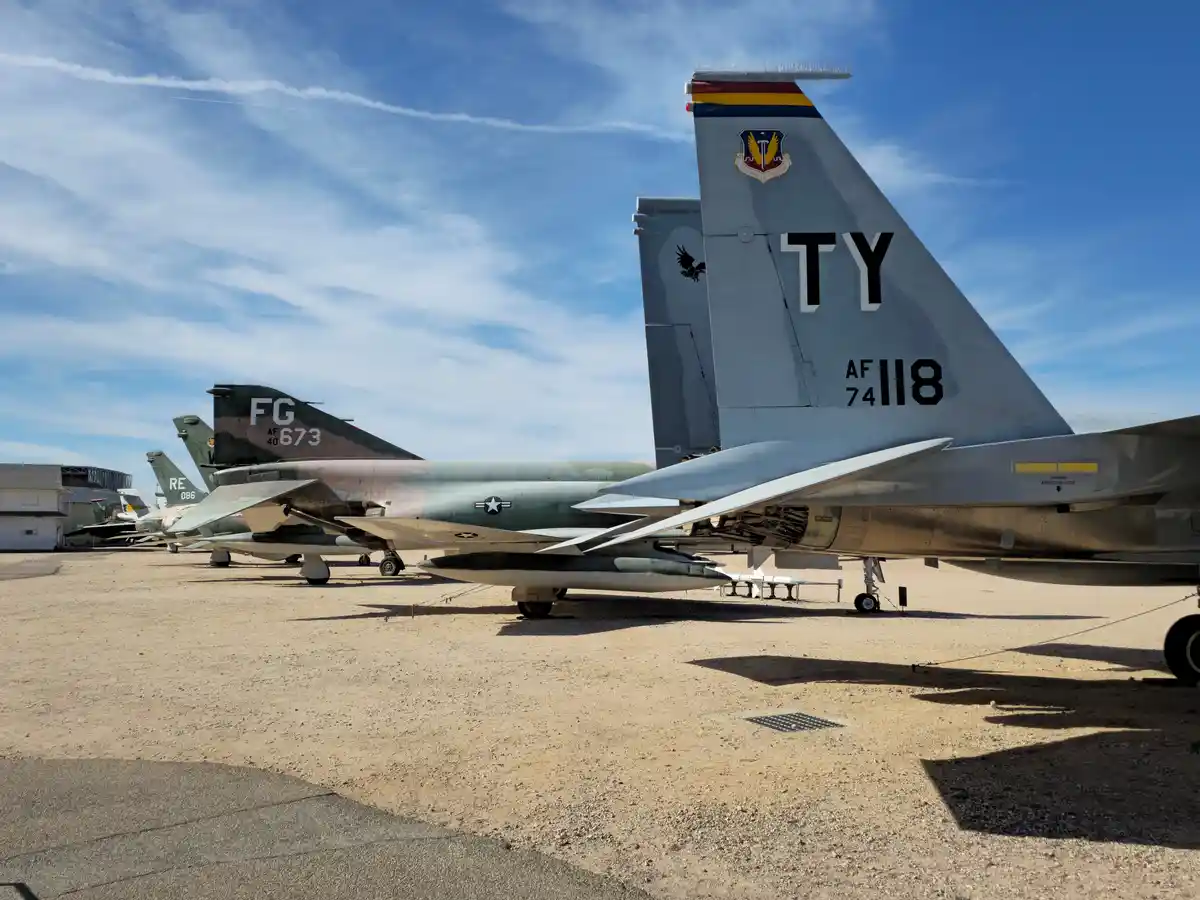 A row of military fighter jets parked outdoors on a sunny day, with the tail of the foremost jet prominently displaying the…