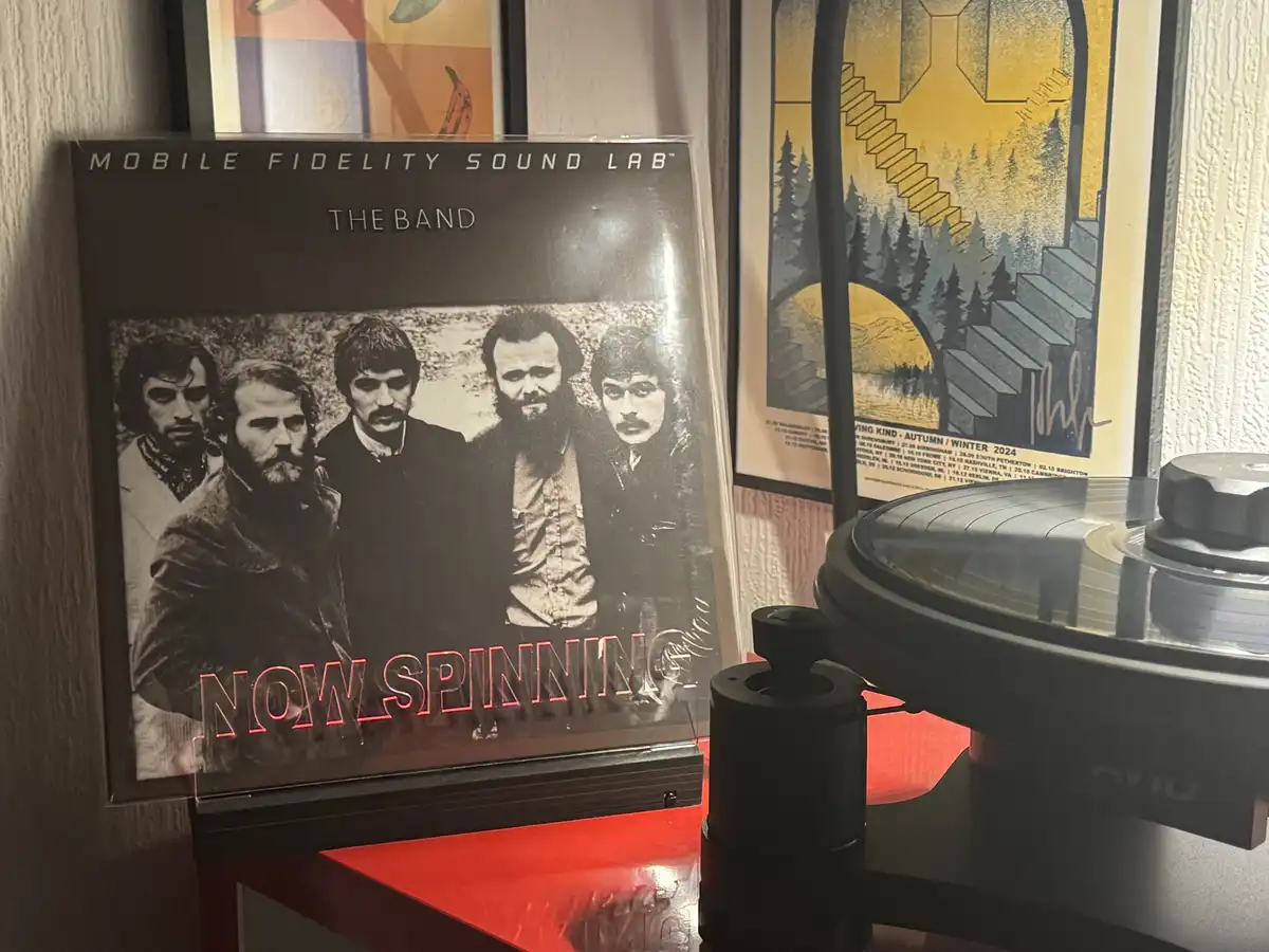 A vinyl record sleeve for 'The Band' by Mobile Fidelity Sound Lab is displayed upright on a red shelf next to a turntable…