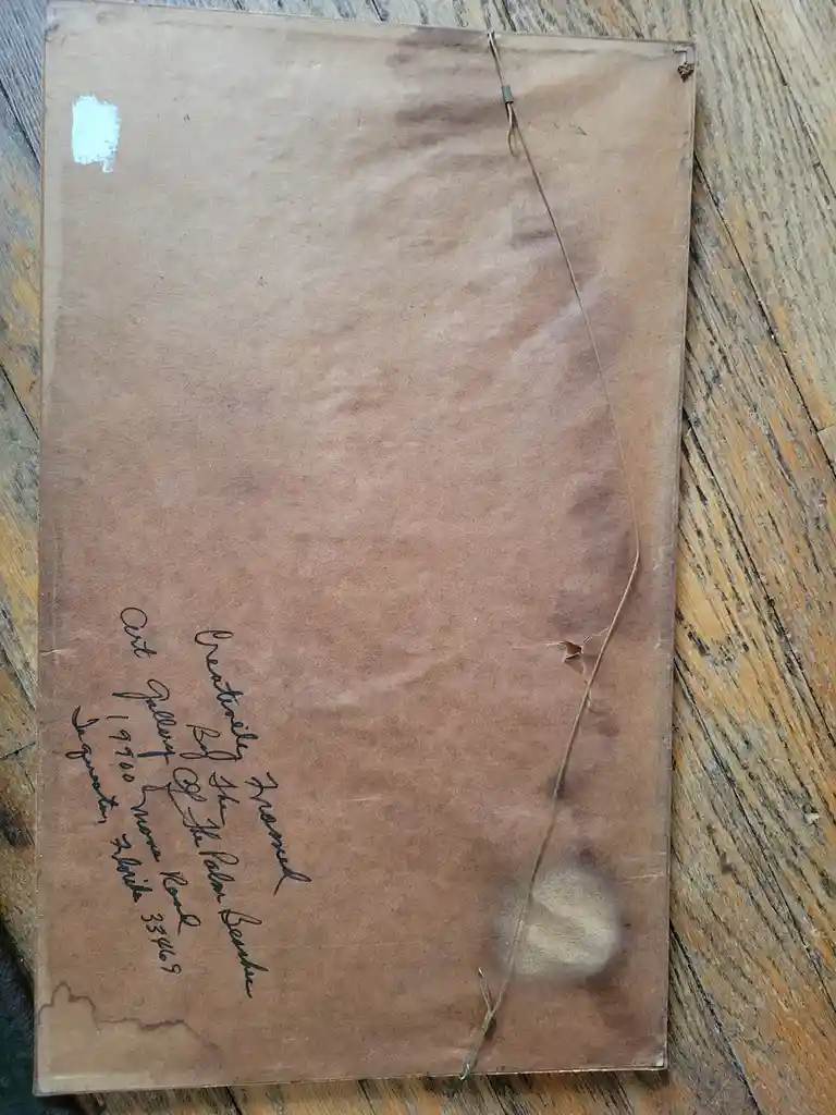 A weathered, brown paper-covered item, possibly a framed artwork or document, lies on a wooden surface. It has handwritten…