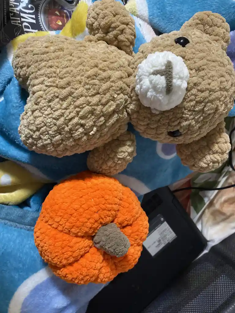 A tan crocheted teddy bear with a white snout and black button eyes is lying on a blue blanket, positioned above a bright…