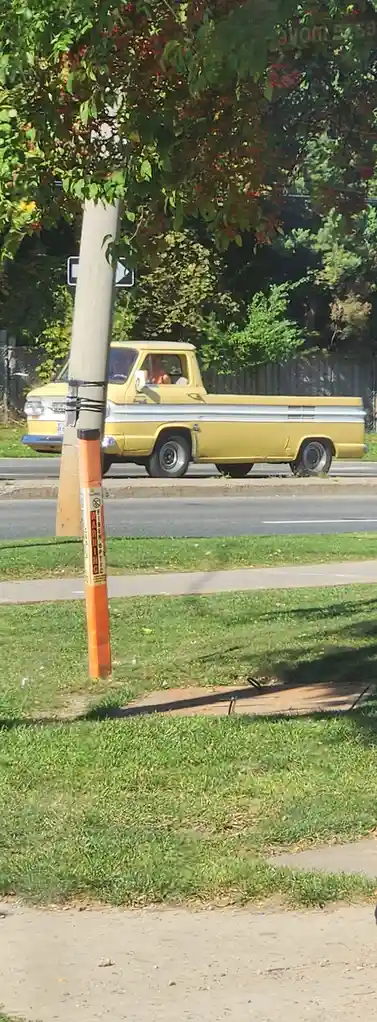 A yellow vintage pickup truck drives past a utility pole with an orange warning label that reads 'WARNING FIBER OPTIC'. The…