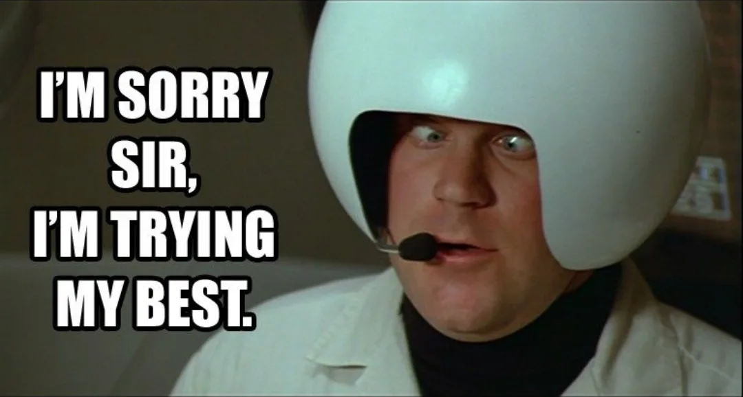 A man wearing a white helmet with a microphone and a white coat looks upward with a strained, apologetic expression. The…