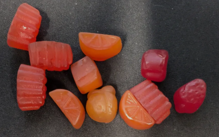 A close-up photo shows several translucent, colorful gummy candies shaped like citrus slices, a bear, and other forms…