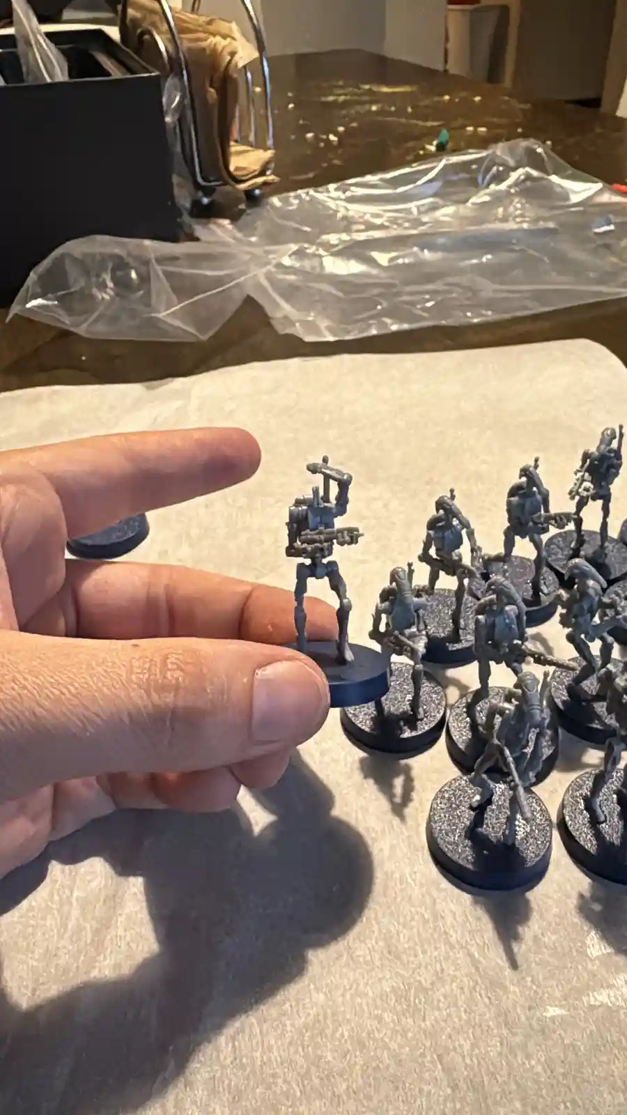 A hand holds up a single unpainted grey miniature soldier figurine, while a group of similarly unpainted miniatures sits on…