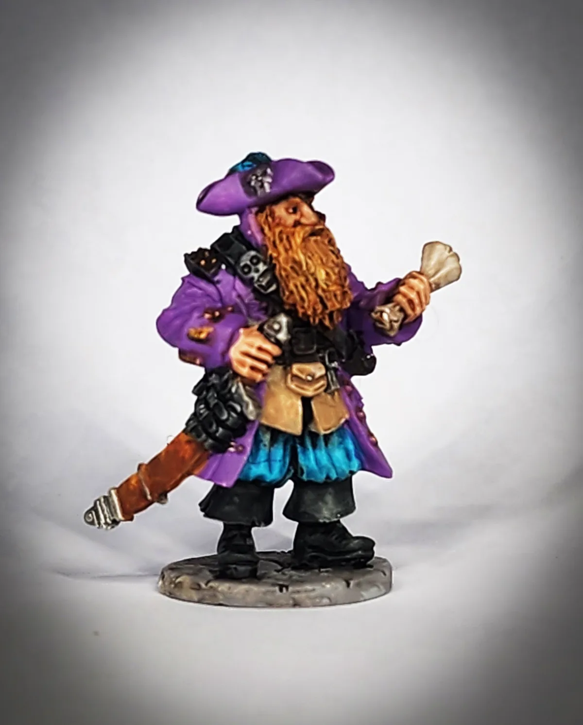 A painted miniature figurine of a bearded pirate wearing a purple coat and hat, holding a bone in one hand and a sword in…