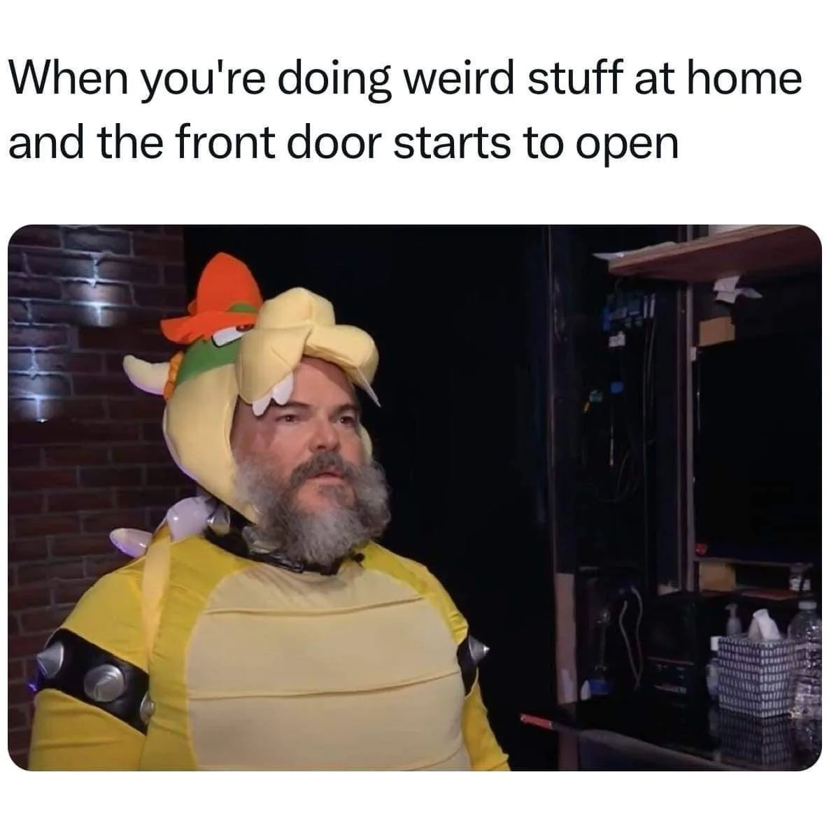 A man with a gray beard wearing a yellow Bowser costume with an orange hat and white horns looks startled, standing indoors…