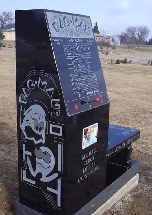 A black tombstone shaped like a classic Pac-Man arcade machine, featuring the game's logo, maze, and character. It includes…