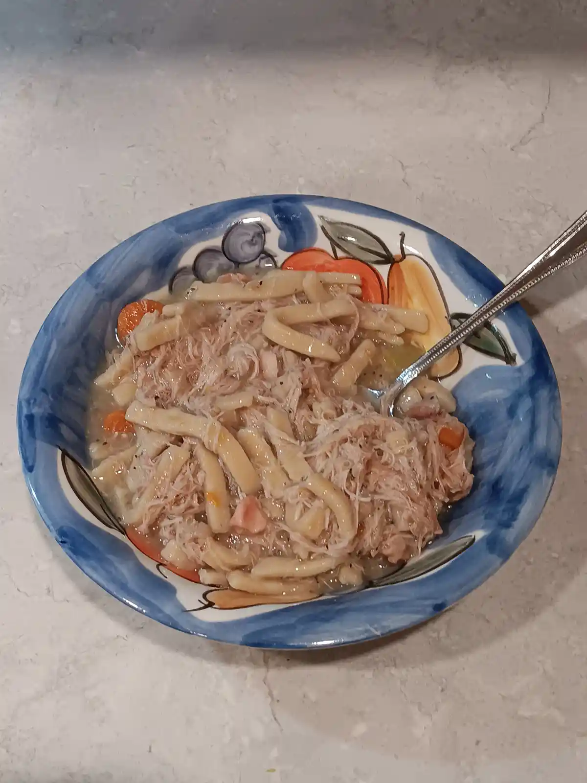 A close-up photo shows a bowl of chicken noodle soup with visible shredded chicken, pasta, and carrots, served in a…