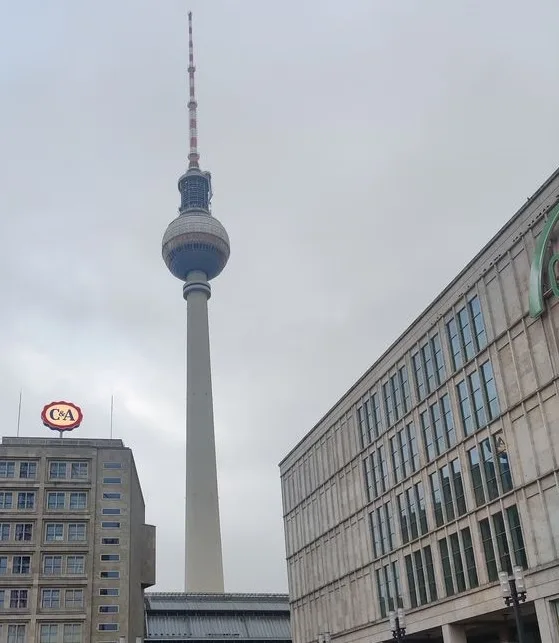 A photo of the Berlin TV Tower (Fernsehturm) towering over city buildings, with a C&A department store sign visible on a…