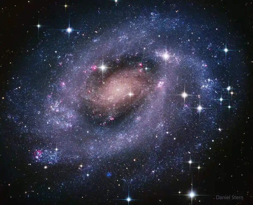 A stunning astronomical photograph of a spiral galaxy filled with countless stars, glowing pink and blue nebulae, and a…
