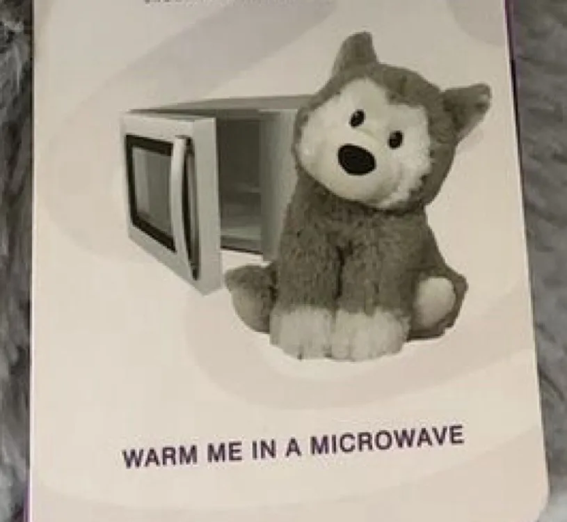 A plush gray and white stuffed wolf sits beside an open microwave on a product packaging insert. The text overlaid at the…