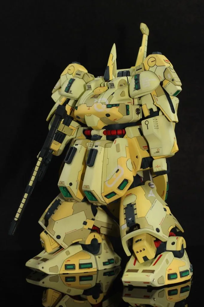 A detailed yellow and cream-colored model of a humanoid mech robot, standing on a reflective surface against a black…