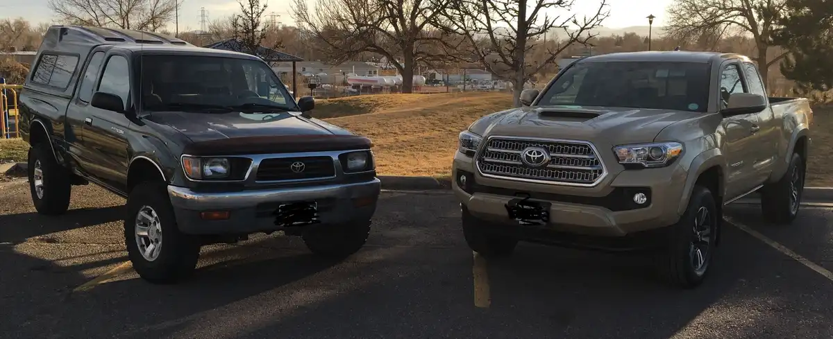 Two Toyota pickup trucks parked side-by-side in a lot: an older, dark gray model on the left and a newer, tan model on the…