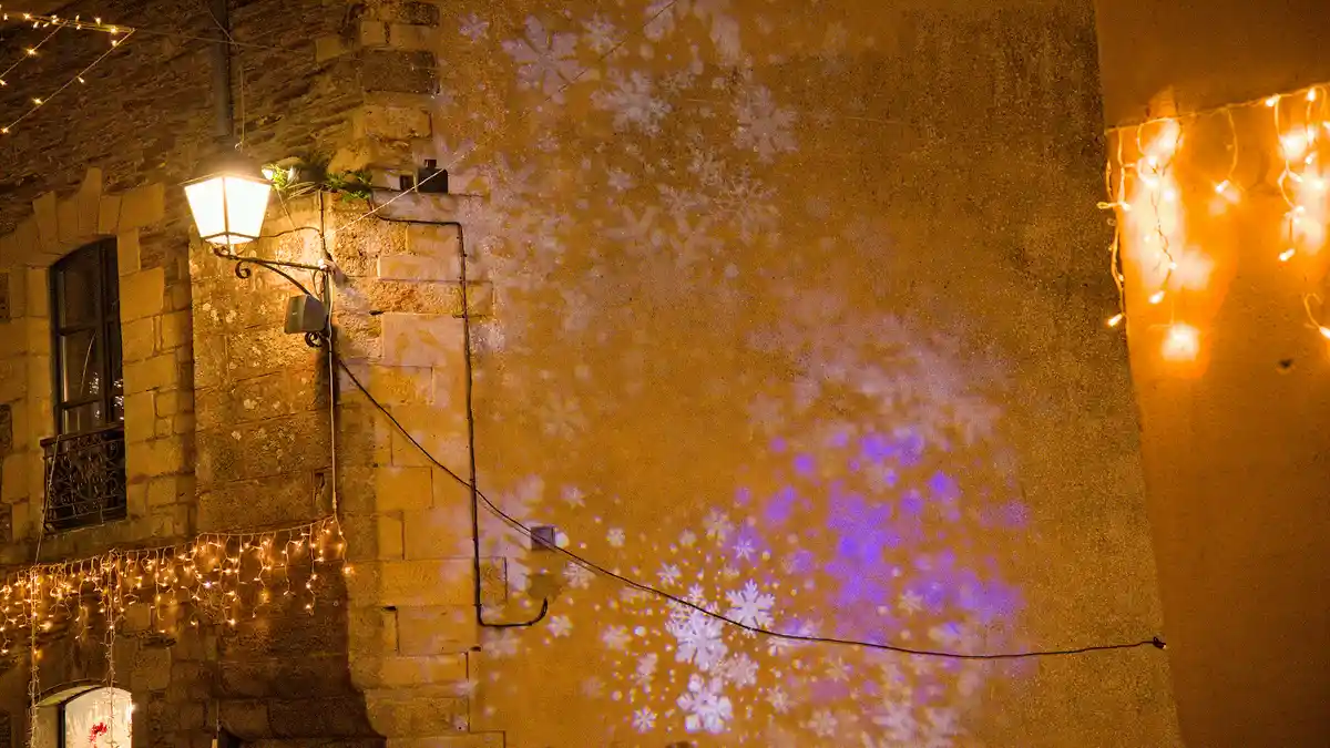 The image shows a repeating sequence of a nighttime scene where snowflake projections in white and purple are cast onto a…
