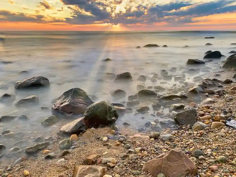 A serene beach scene at sunset with calm, misty water and scattered rocks, overlaid with the text 'i'm not lazy, i'm in…