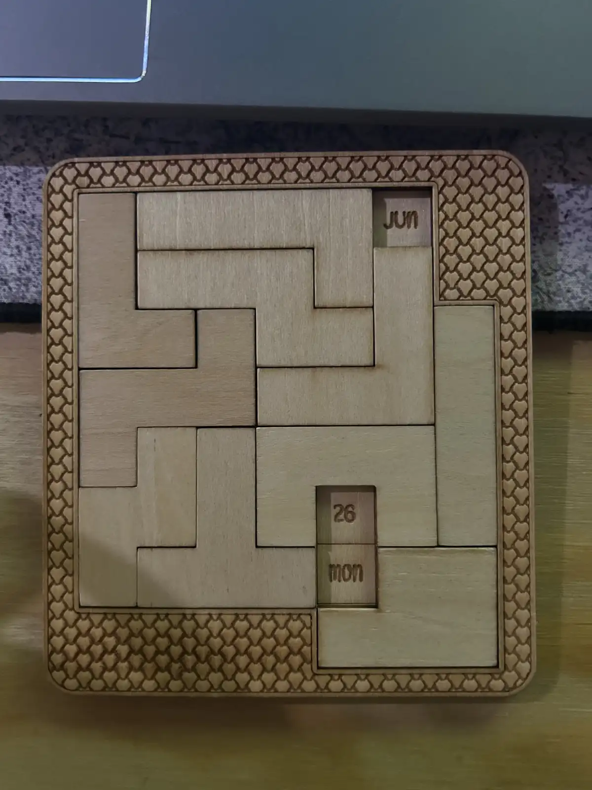 A wooden puzzle calendar with interlocking pieces forming a grid, showing 'jun' in the top right and '26 mon' in the bottom…