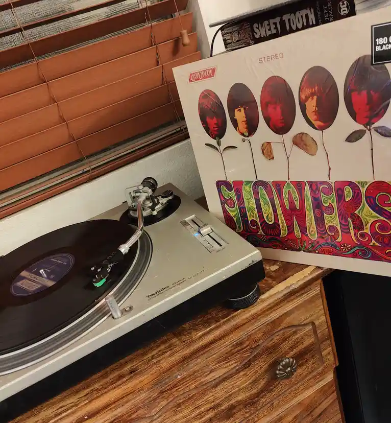A Technics turntable sits on a wooden dresser next to the 'Flowers' album by The Beatles, whose cover art features four oval…
