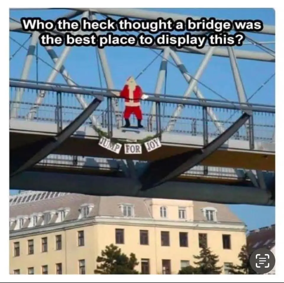 A large, cartoonish Santa Claus figure is mounted on the railing of a modern metal pedestrian bridge, with a banner below…
