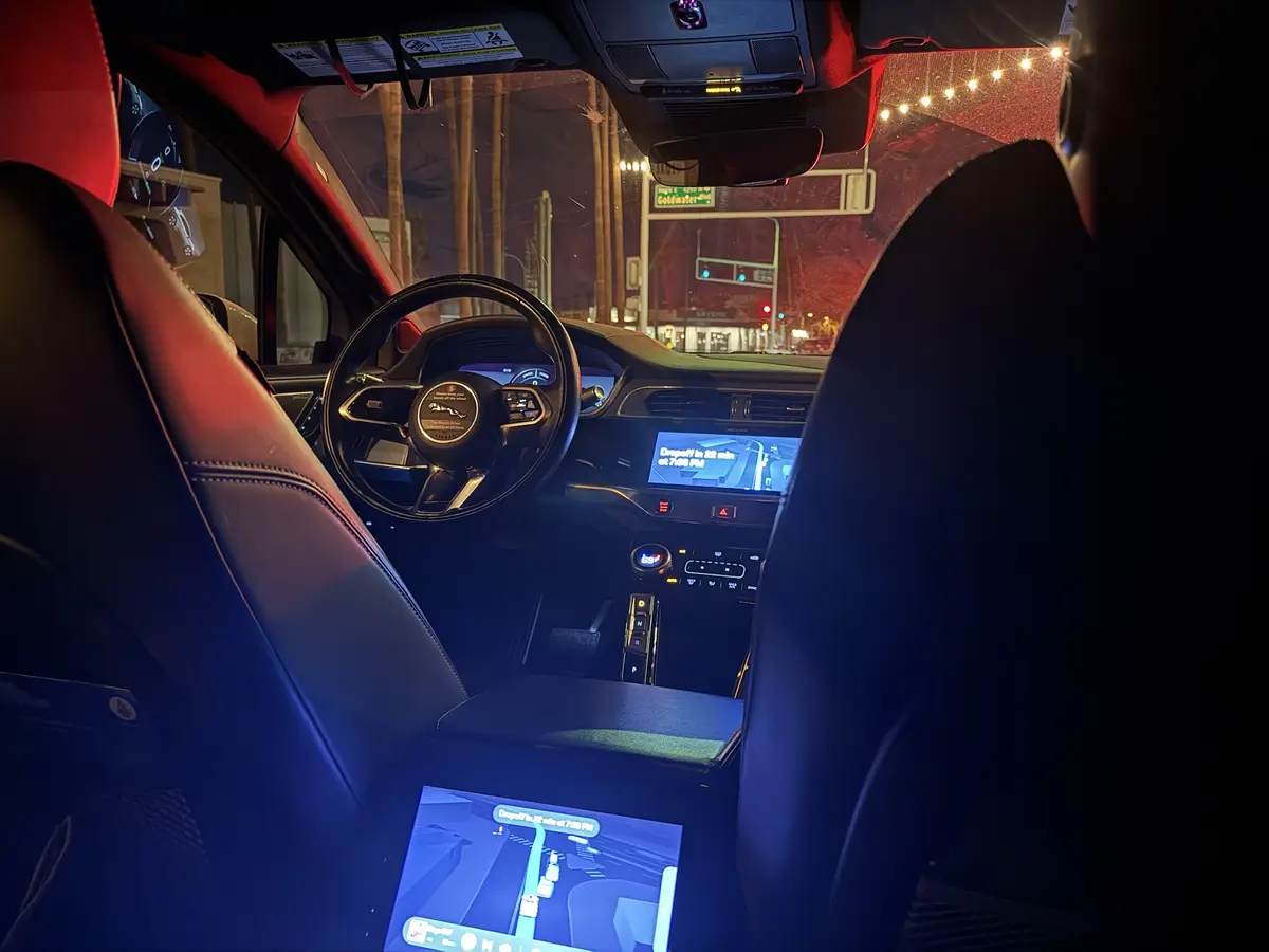 A nighttime photo from inside a Jaguar taxi, showing the driver's seat, steering wheel, and dashboard. The car's…