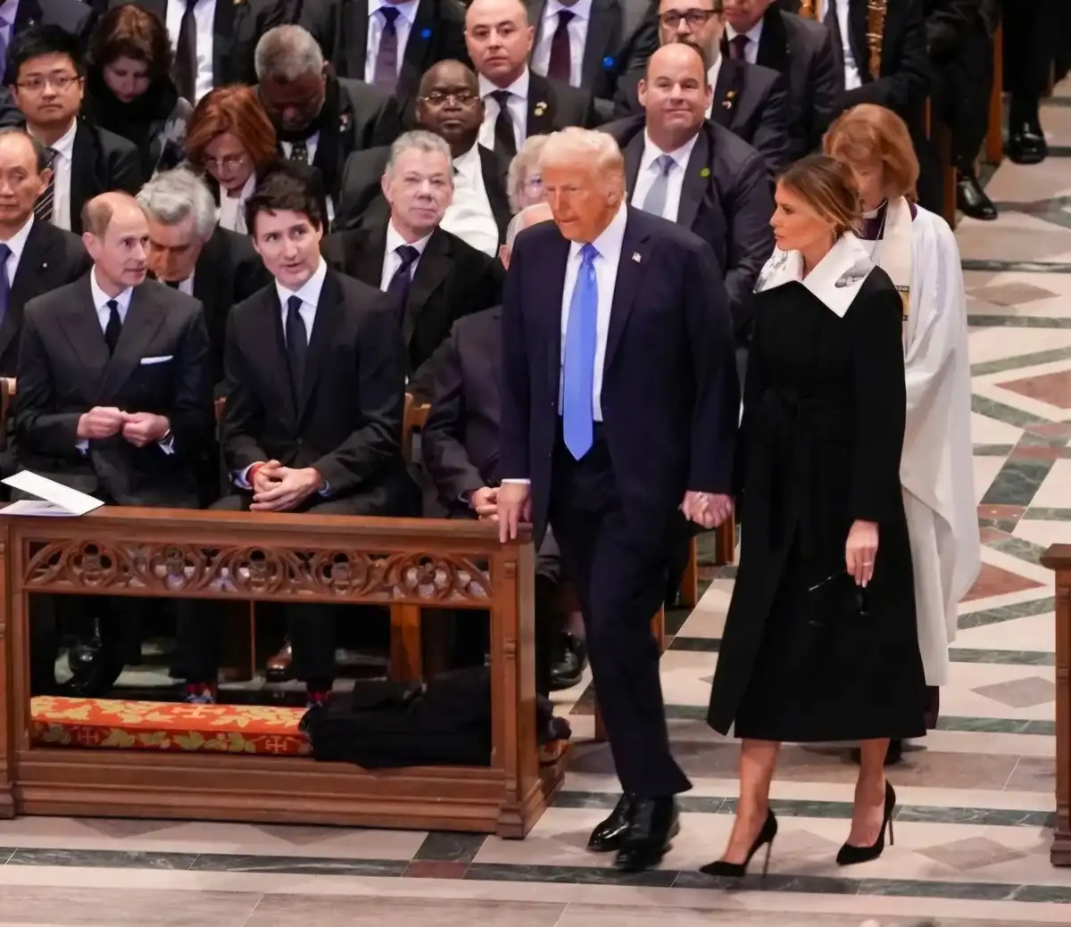 A photo shows Donald Trump and Melania Trump walking through a church, holding hands, while seated world leaders including…