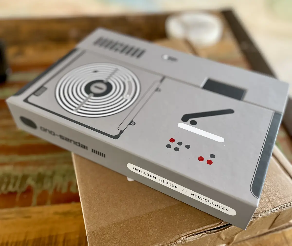 A gray book box designed to look like a retro-futuristic computer or console, featuring a circular interface, red and black…